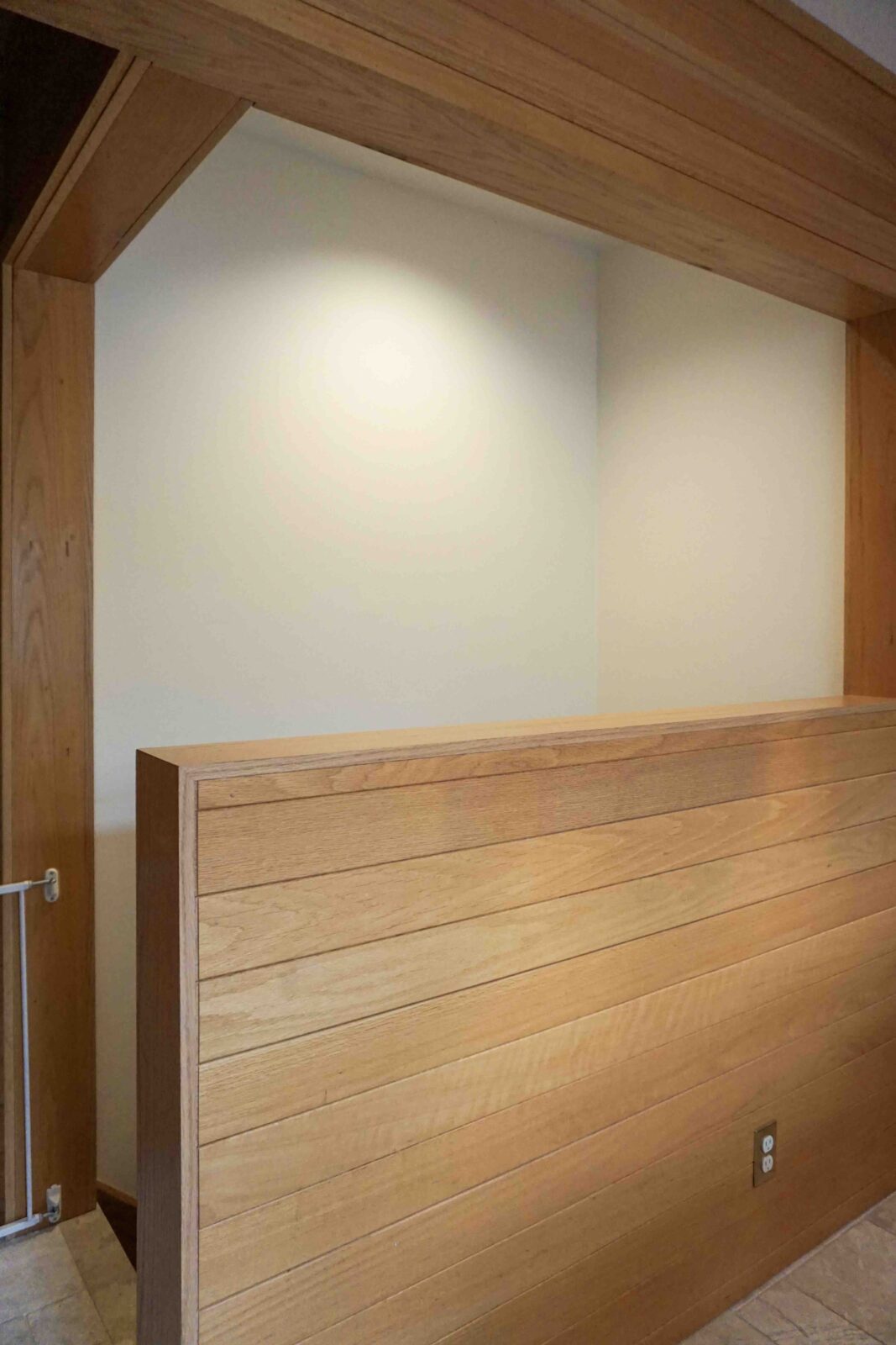 The top of a basement stairwell with white walls and a wood-paneled half wall in the foreground