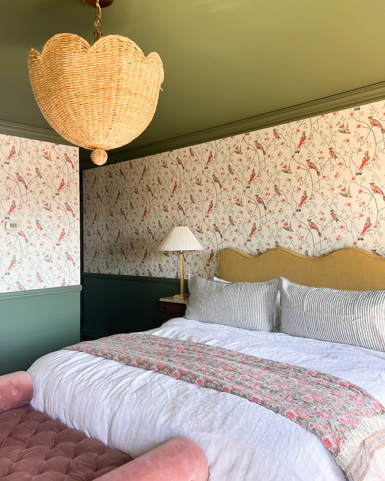 Angled view of a bedroom with a patterned wallpaper, patterned quilt and chaise.