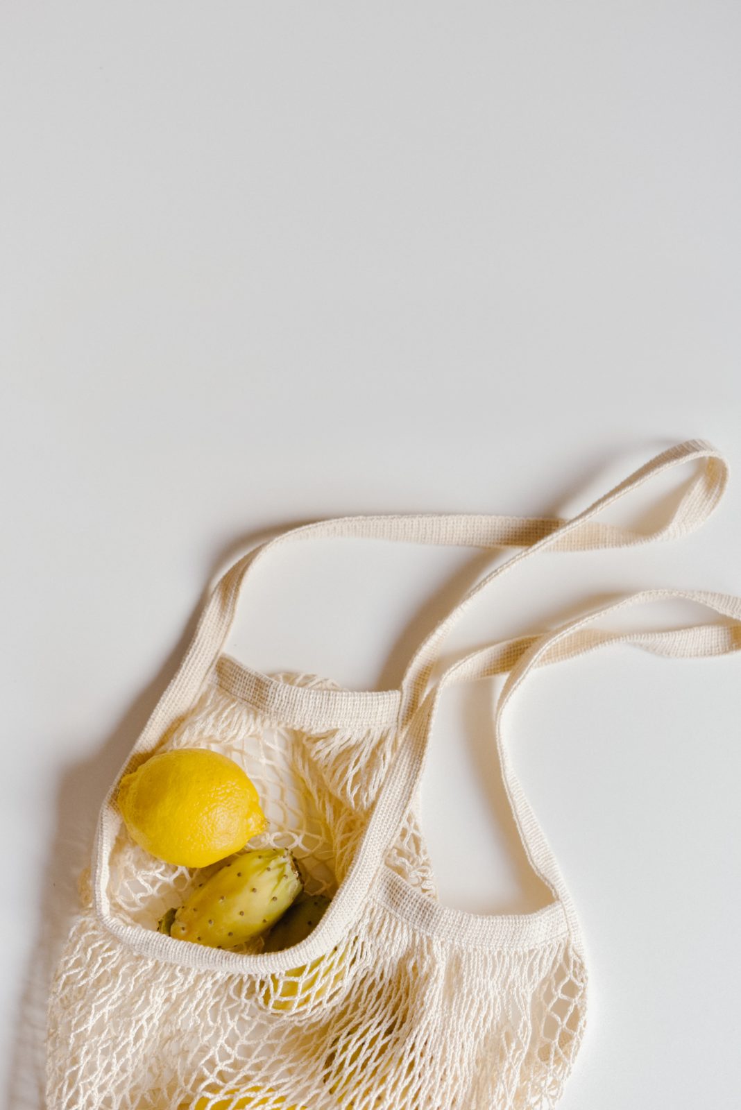 A reusable bag lies on a white surface with lemons and seasonal fruit inside