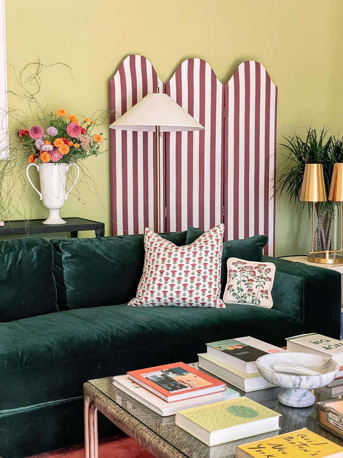 Family room with green walls, a green velvet sofa, modern lamps, a red and white striped screen, and a coffee table with books atop it.