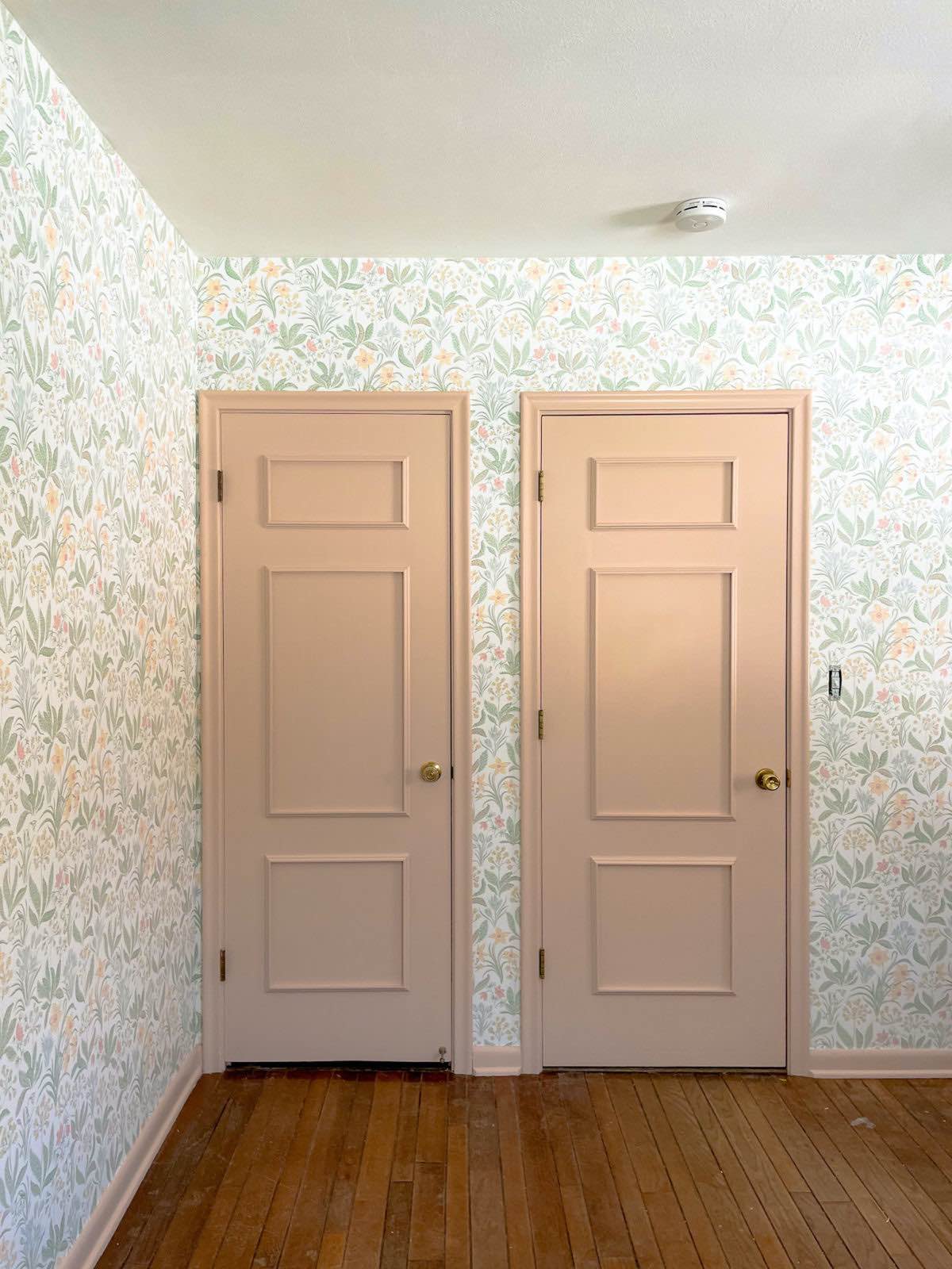 Guest room design. Two doors in a small room with a white ceiling and wood floors. Sandberg Huset i Solen Spring Green wallpaper and Setting Plaster by Farrow & Ball paint. 