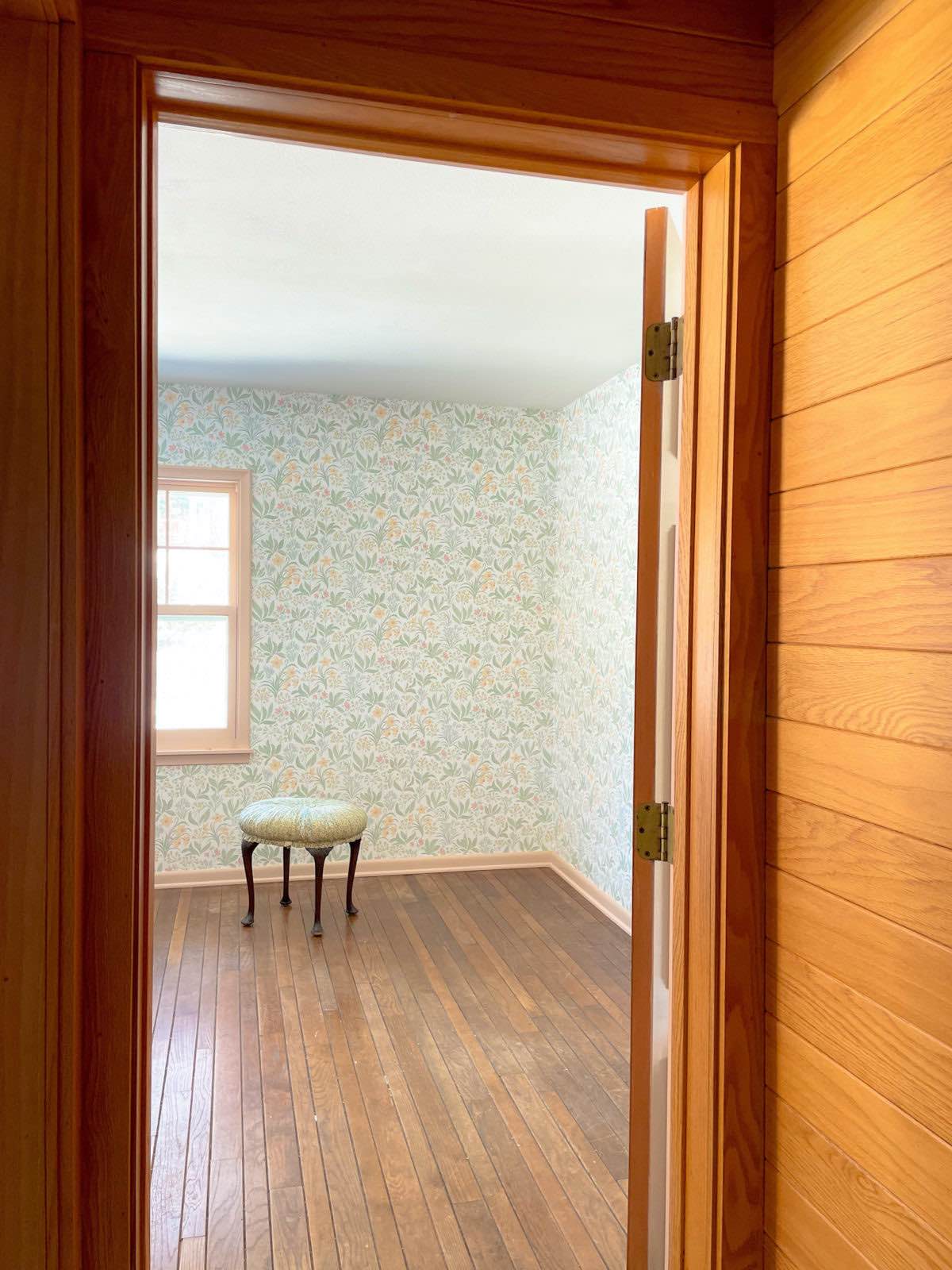 Looking into a guest room with wood floors, Sandberg Huset i Solen Spring Green wallpaper, and Setting Plaster by Farrow & Ball painted trim