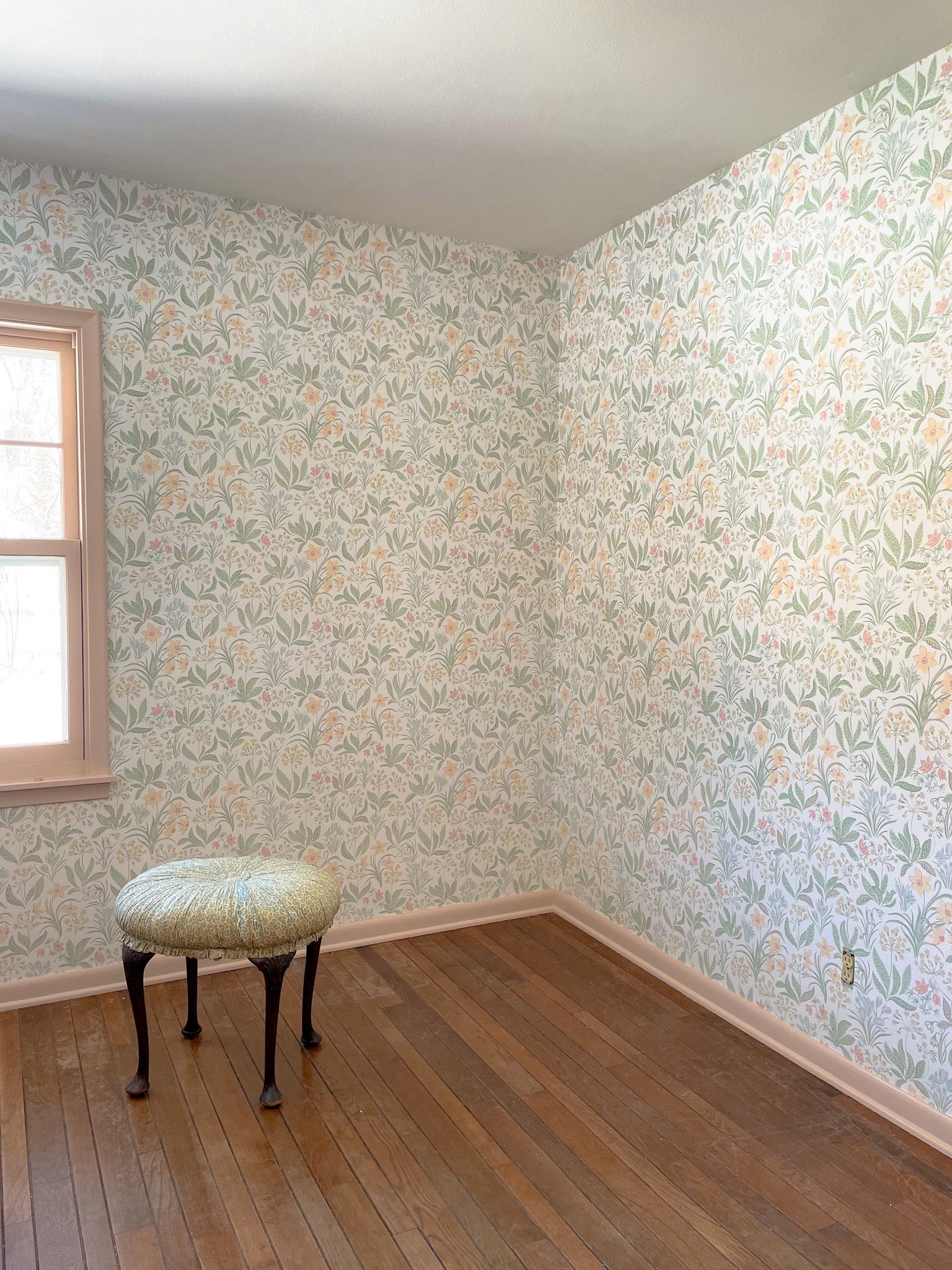 A guest room with wood floors, Sandberg Huset i Solen Spring Green wallpaper, and Setting Plaster by Farrow & Ball painted trim