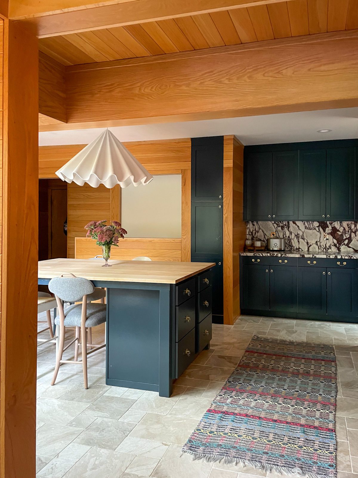 Kitchen dining area with navy blue cabinets, wood paneling, marble floors and countertops, an island, and a white pendant light.