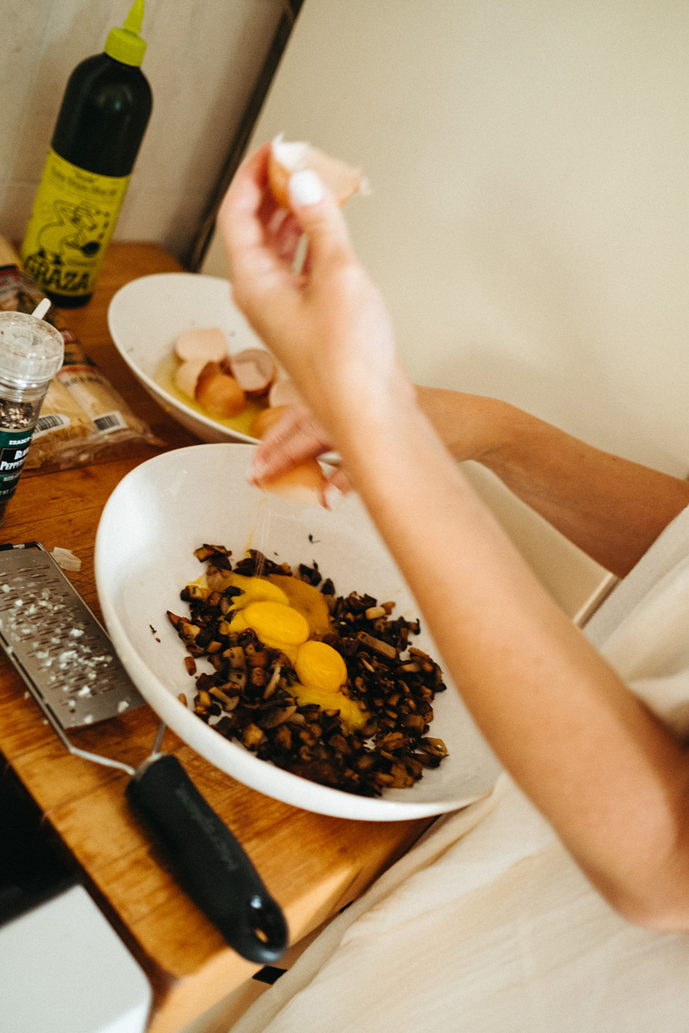 A creamy mushroom pasta is being prepared. Cooked mushrooms and egg yolks are being mixed in a large serving bowl sitting on a wooden countertop.