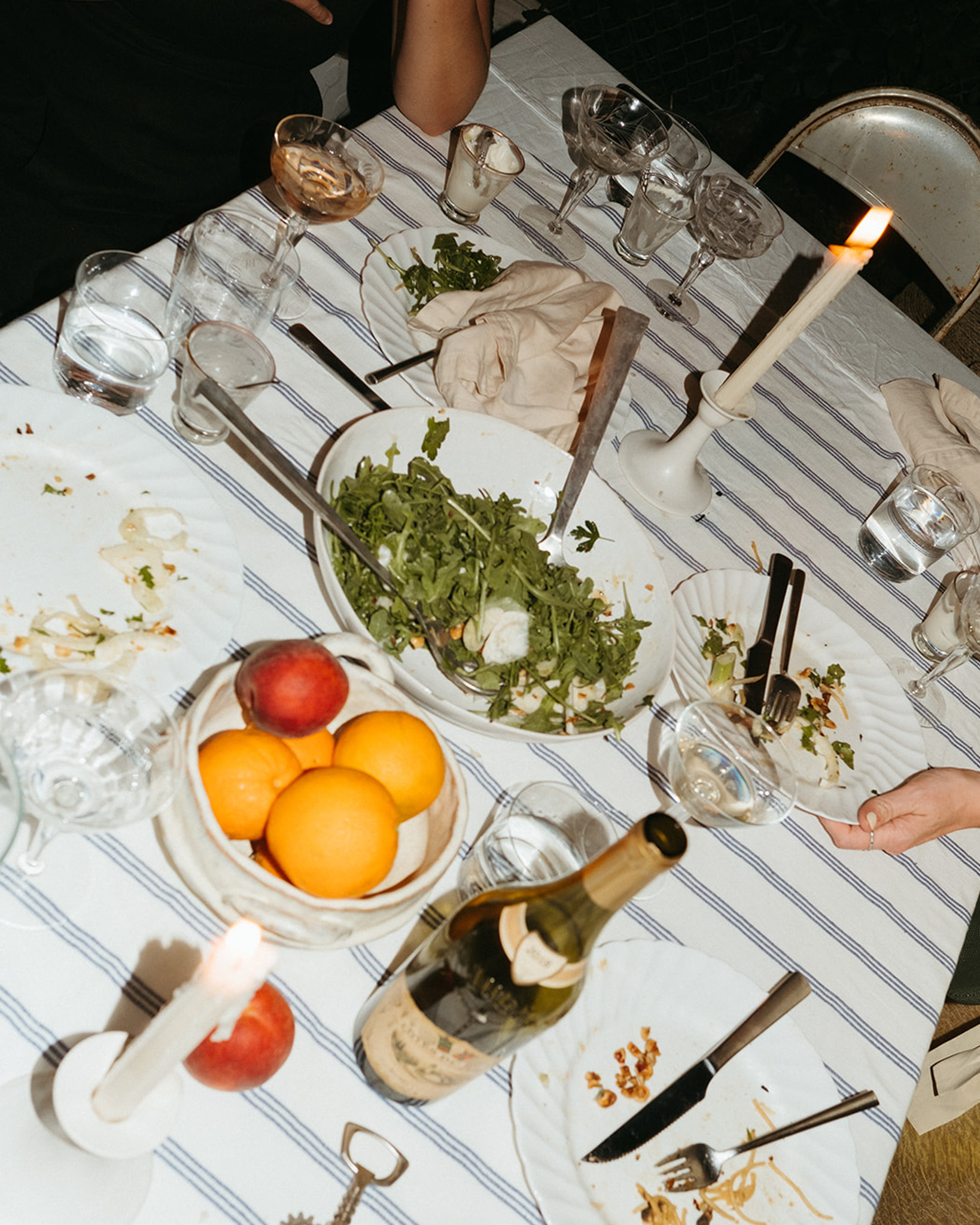 The table after a casual dinner party is shown with empty plates, an open bottle of wine, and dripping tapered candles.