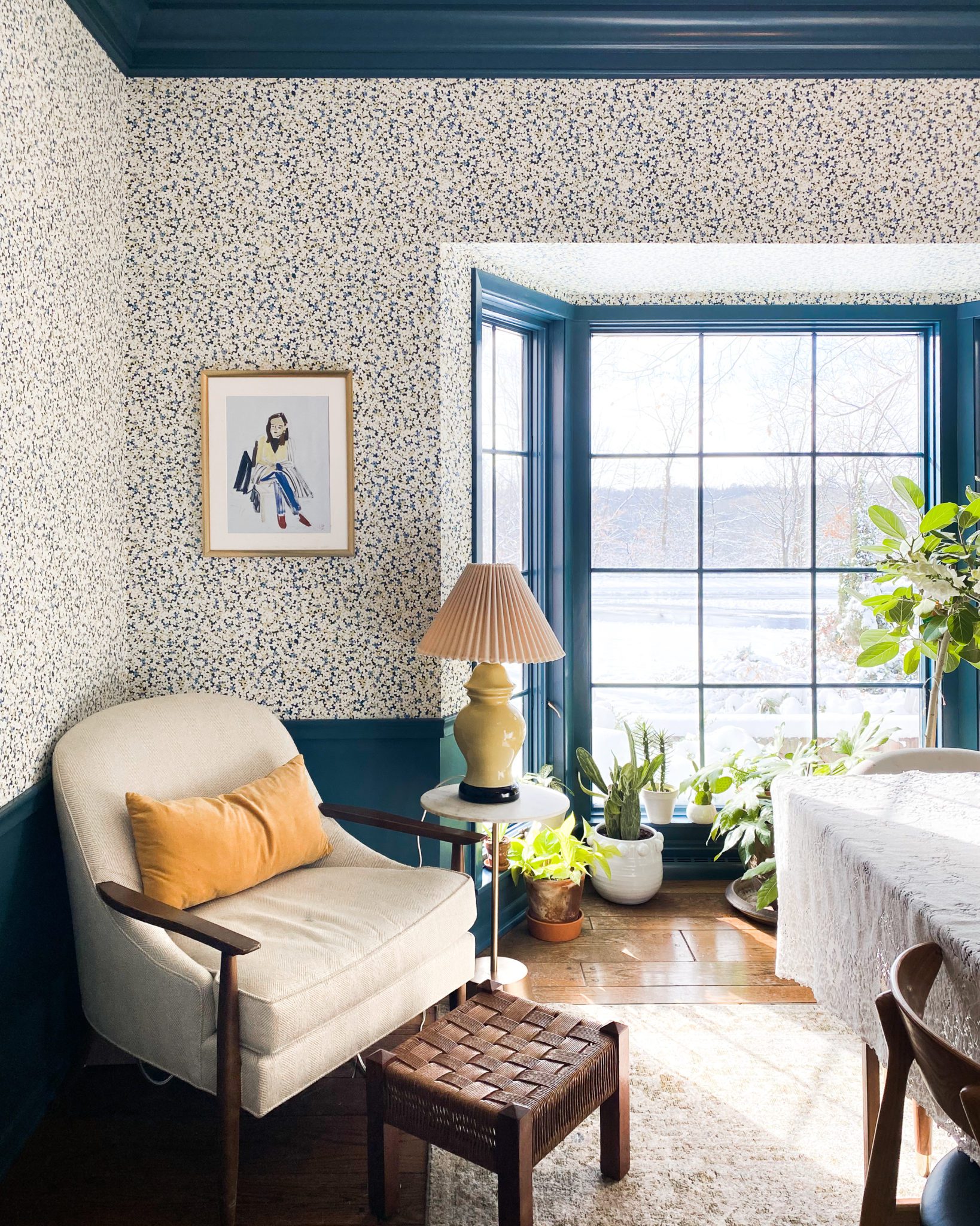 A white chair with a yellow pillow. Chair is in a library with blue walls and floral wallpaper.