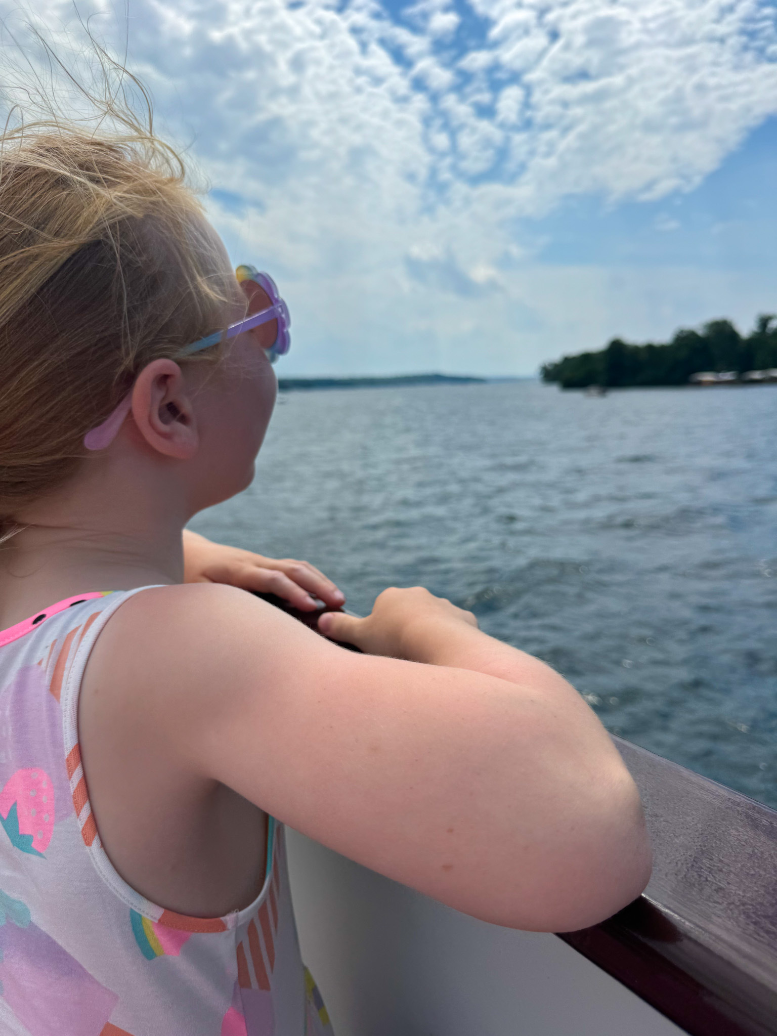 A kid wearing flower sunglasses looking out over a lake in the summer