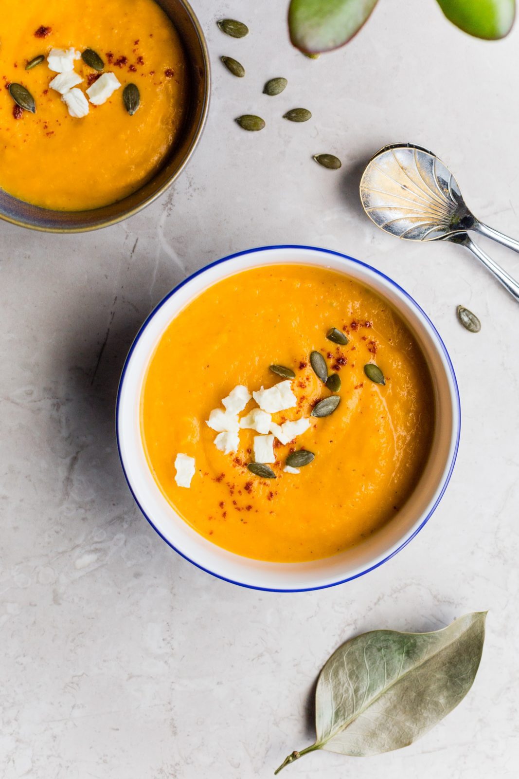 Fall Soup Recipes: Two bowls of orange pureed soup are topped with spices, cheese, and pumpkin seeds.