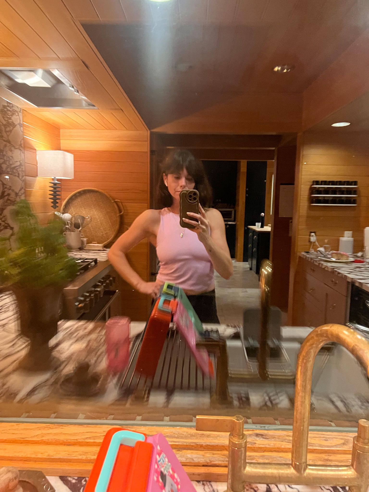 A woman stands in front of her kitchen sink in the early morning hours, wearing a pink tank top and leggings