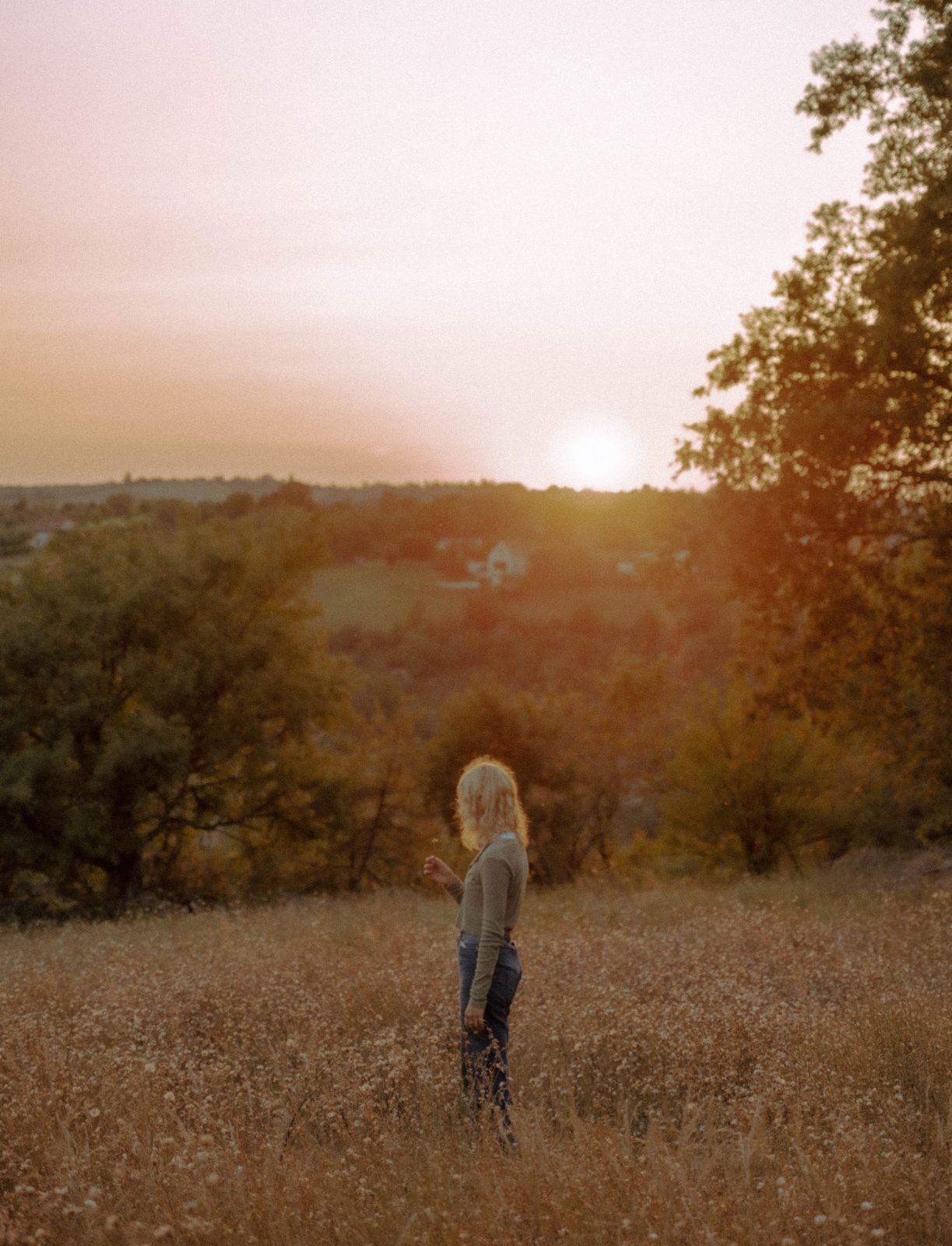 Mental health. Woman standing in an open field looking over a hillside at sunset.